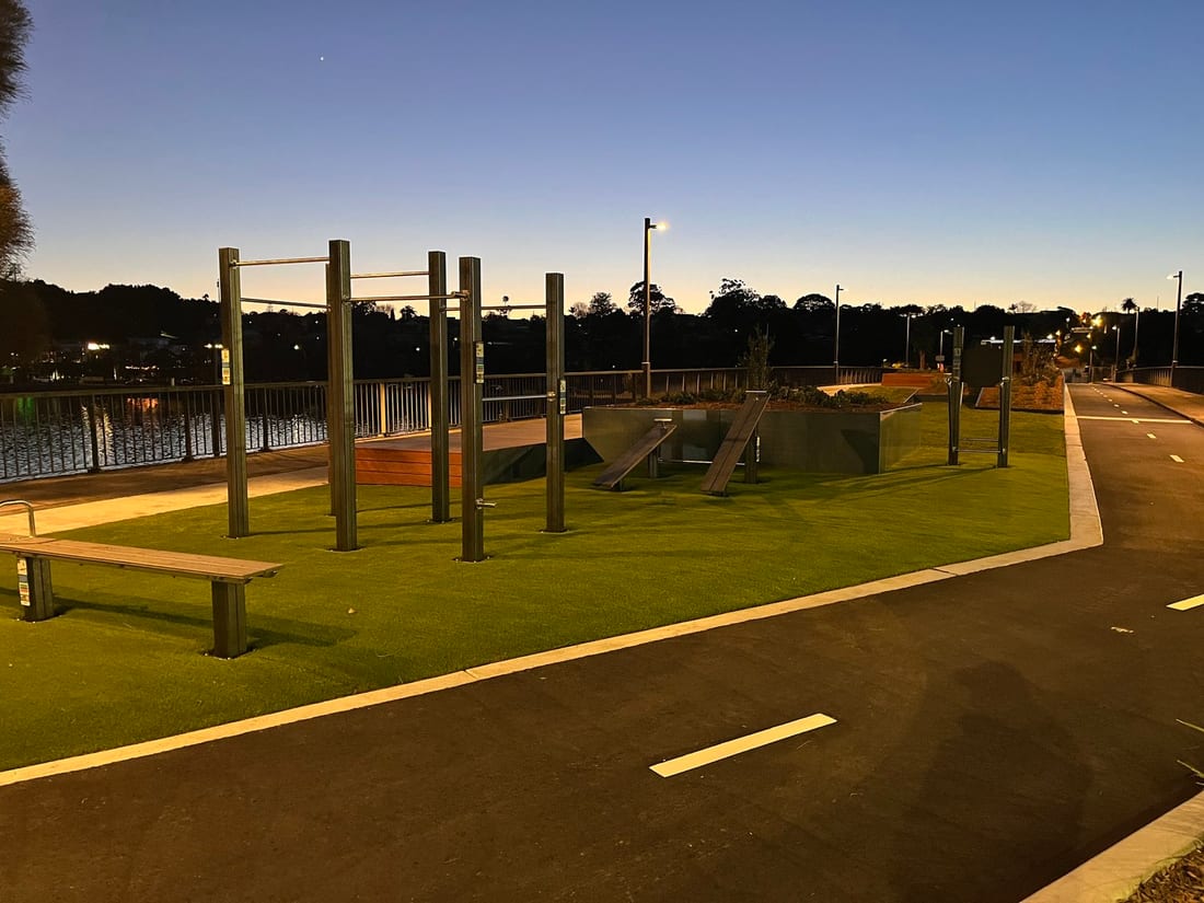 Outdoor fitness station and lit foreshore precinct at dusk on the Bay Run
