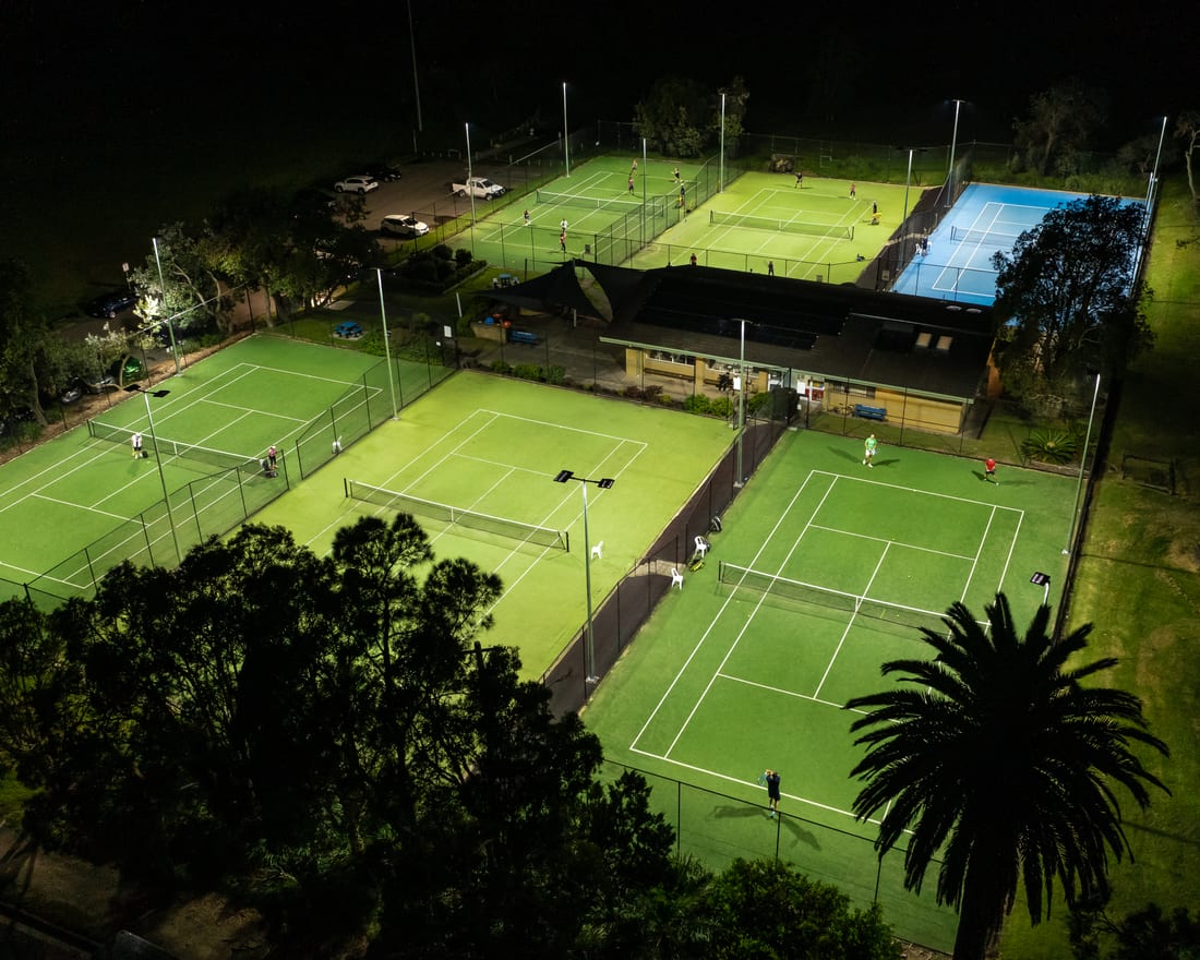 Low aerial of the lit Collaroy tennis courts at night with players