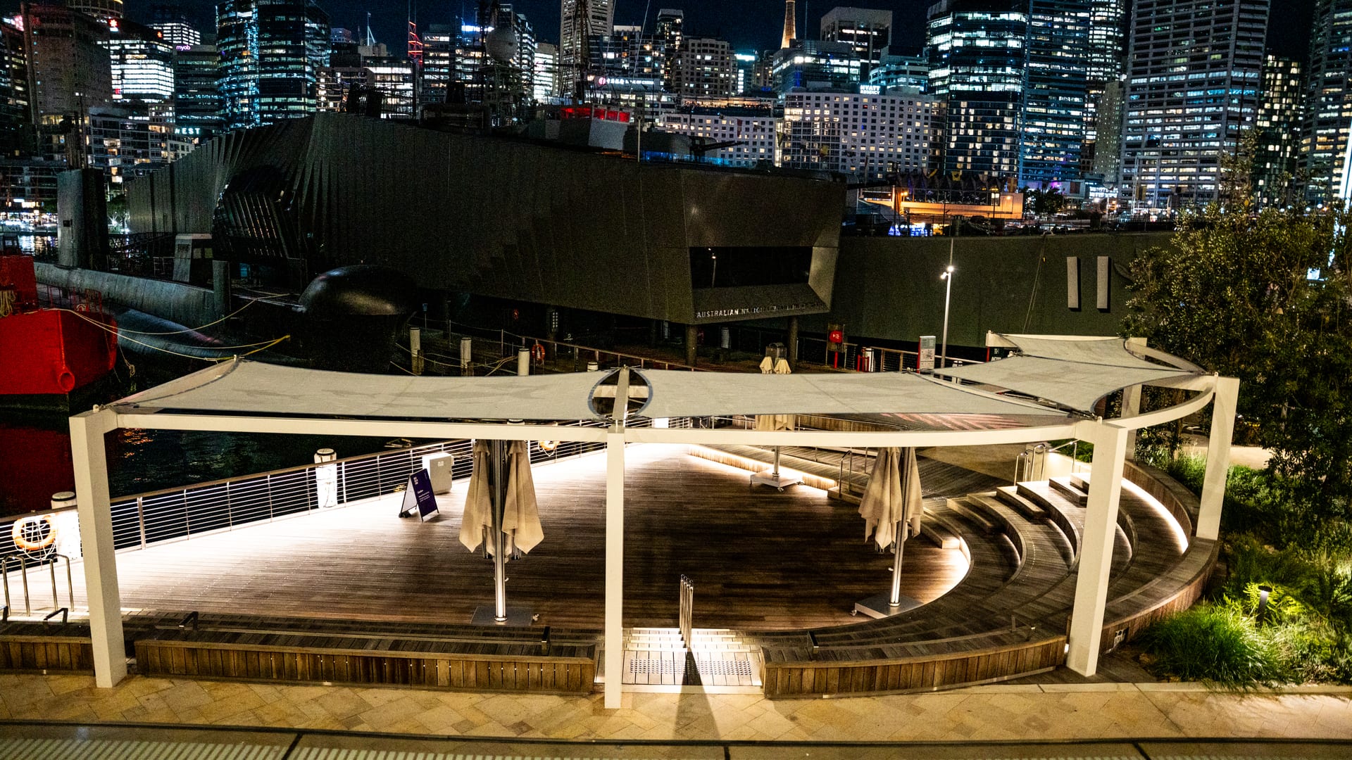 Floodlit harbour-edge boardwalk and terrace at the Australian National Maritime Museum at night