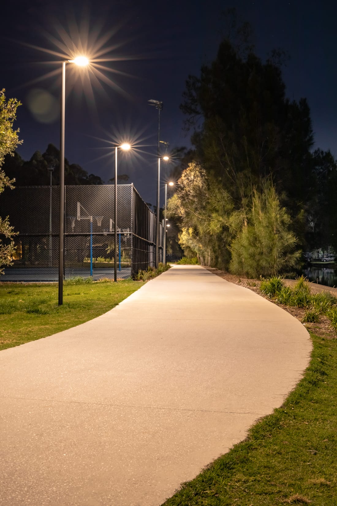 Illuminated pathway past the sports courts at Richard Murden Reserve at night